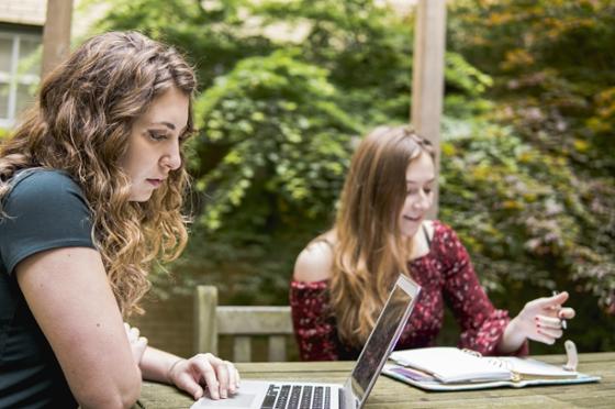 两名波胆网站(Chatham University)的学生坐在外面的一张小酒馆桌旁，用笔记本电脑独立学习. 