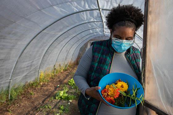 Photo of a female Chatham University student holding a bowl of harvested produce at the door of a greenhouse on 伊甸堂校园