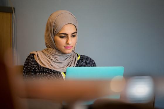 图为一位戴着头巾的波胆网站女学生在咖啡厅里用电脑工作