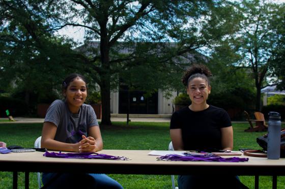 图为两名波胆网站的女学生在桌子后面对着镜头微笑, 在活动会上