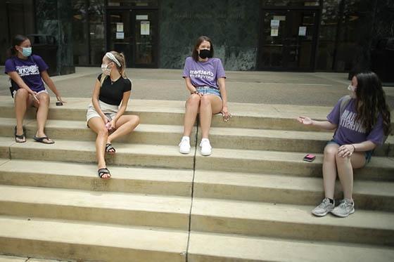 四名波胆网站学生的照片，戴着面具，坐在图书馆的台阶上