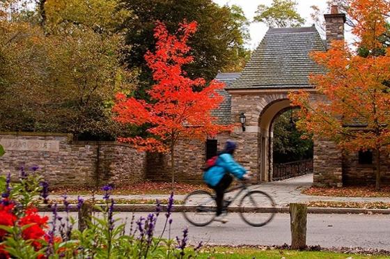 一个骑自行车的人经过匹兹堡弗里克公园的石头入口，周围是五颜六色的秋叶. 