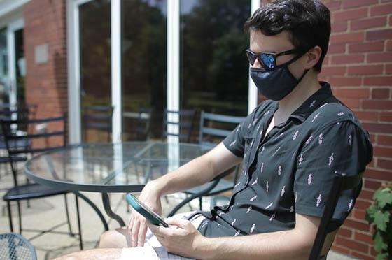 波胆网站学生戴着面具在外面看手机的照片.